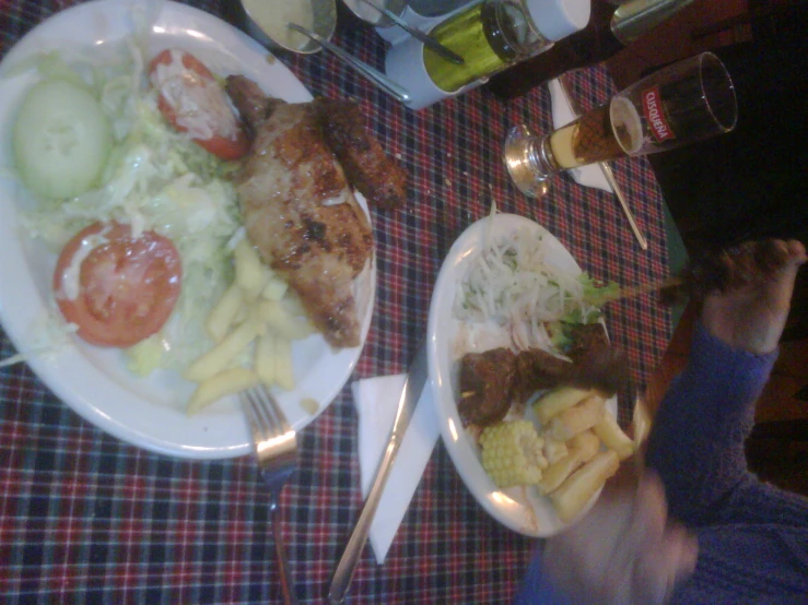 two plates with chicken, salad, french fries, and tomato slices