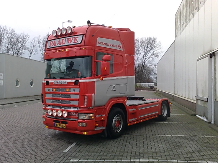 red and grey truck on paved area near buildings