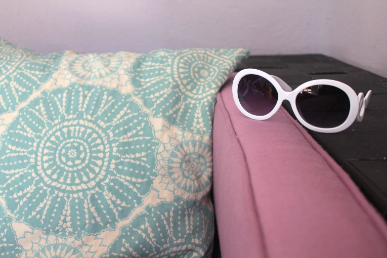 a pair of white sunglasses laying on a pink pillow