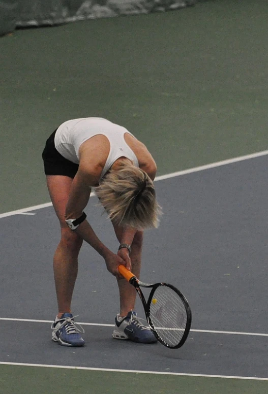 a woman bending down holding a tennis racquet on top of a court