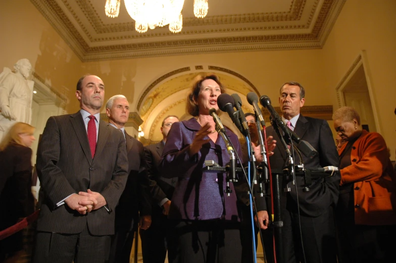 a group of people stand with microphones as two men talk behind them