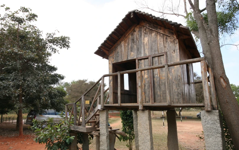 a small wooden structure with wood windows in front of a tree