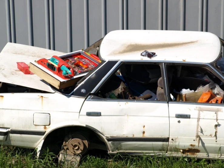 an abandoned white car is parked outside with its hood open