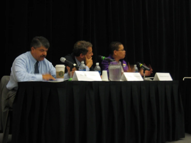 the men sit at tables while talking into microphones