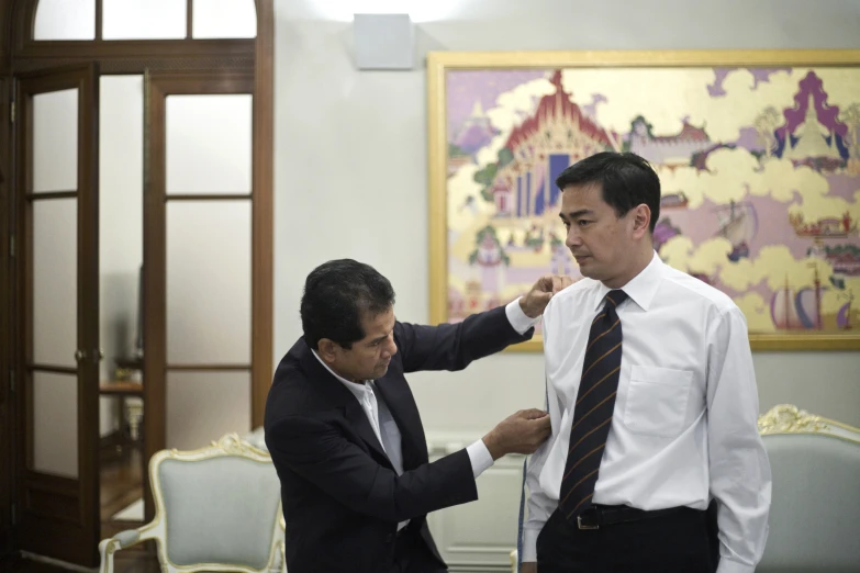 two men standing in front of a table helping each other tie their collars