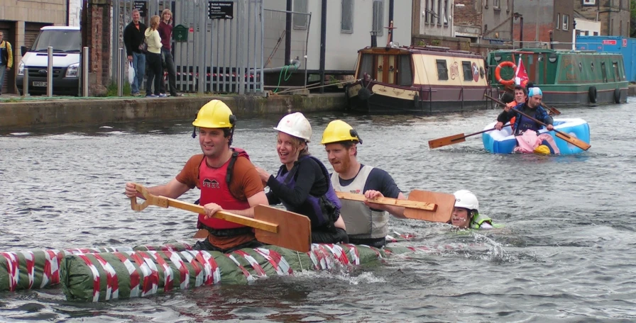 four people in yellow helmets on a boat with one rowing towards the camera