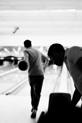 two men are bowling and some is standing by the lanes