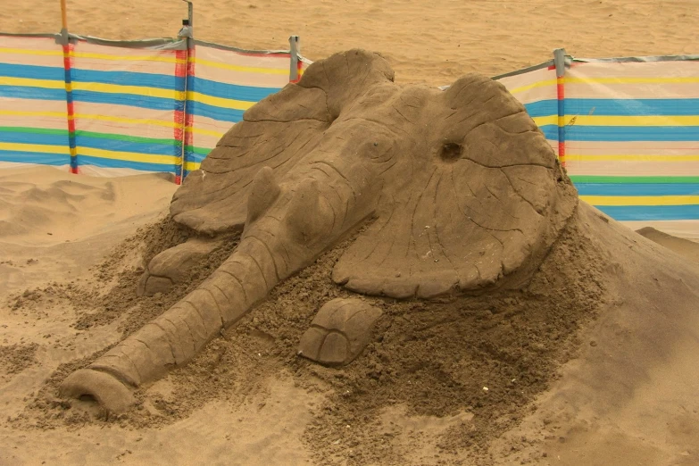 an elephant shaped sand sculpture sitting on top of a beach