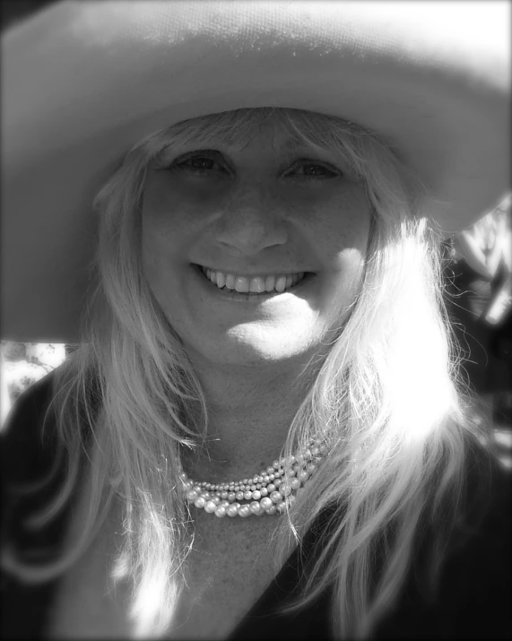 a woman smiling for a picture wearing a hat and pearls