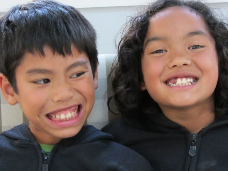 two children in black sweatshirts smiling together