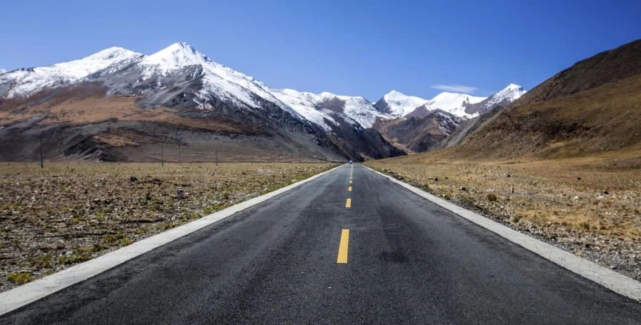 an empty highway surrounded by snow - covered mountains