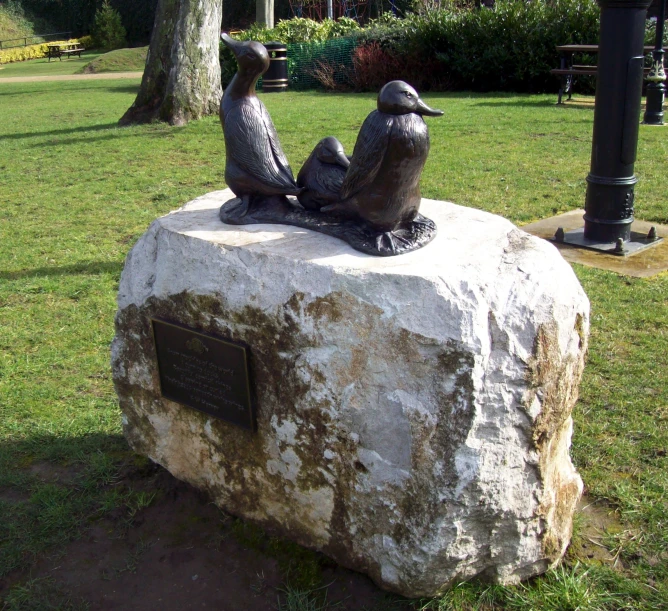 a statue of two birds on a rock with a park in the background