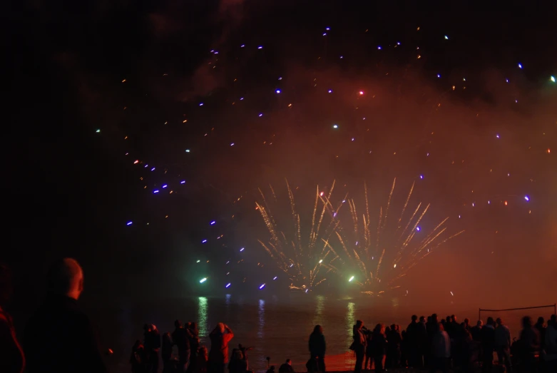 a group of people standing near water watching fireworks