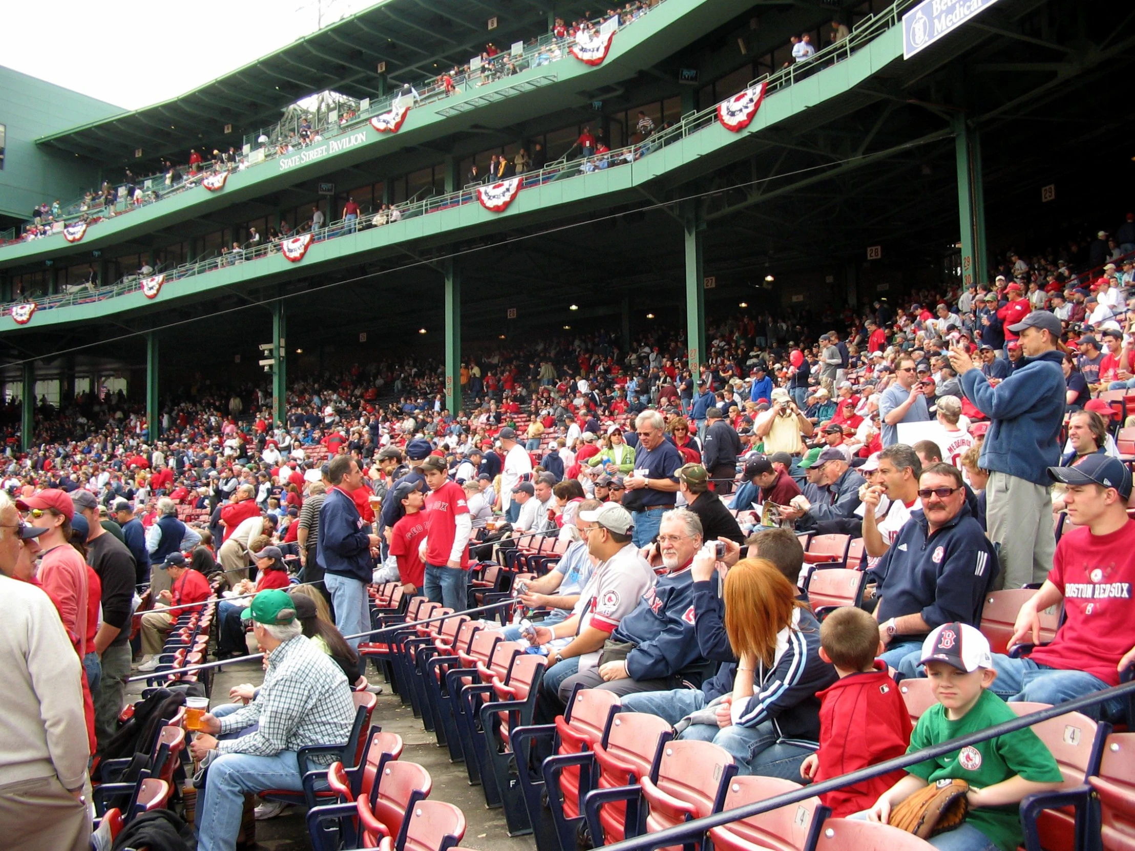 several people sit in an empty stadium while the crowd looks on