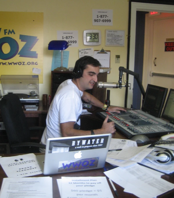 man sits in front of laptop surrounded by papers and recording equipment