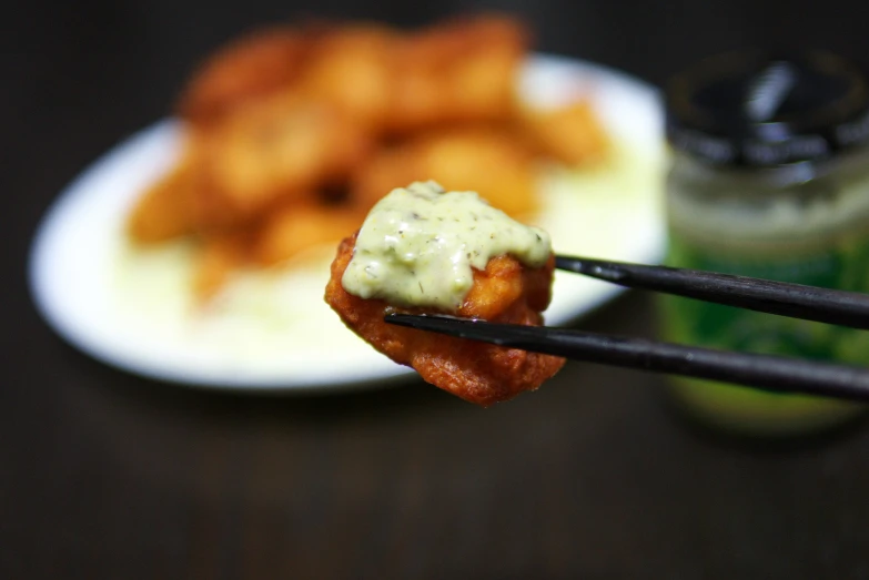 chopsticks holding food in front of a plate of fried chicken nuggies