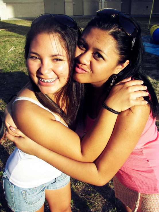 two girls are hugging on the grass together