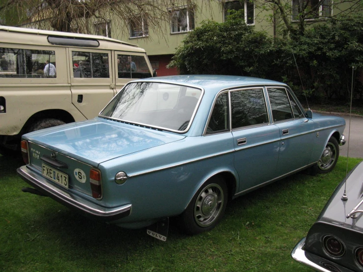 blue car parked in the grass near a bus