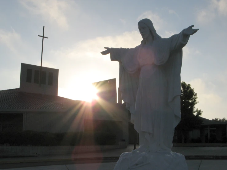 a statue is standing with his hands outstretched, while the sun shines brightly behind