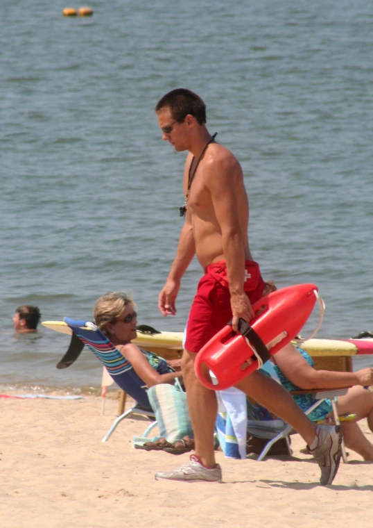 a shirtless man walking on a beach near a man with a life vest