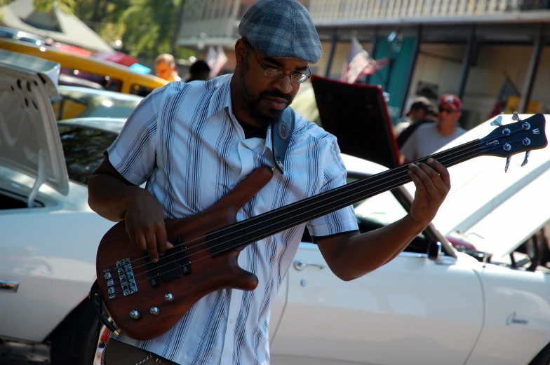 a man standing next to a parked car holding a bass guitar