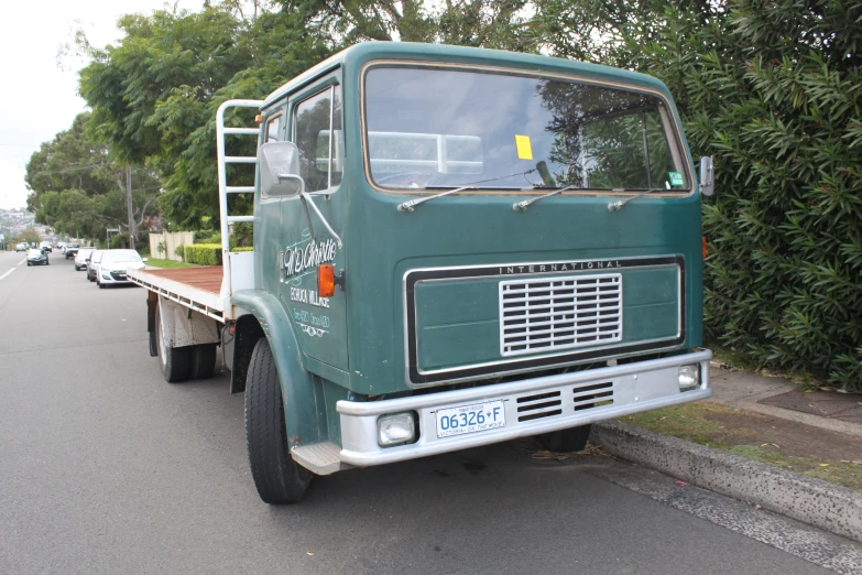 an old green work truck is parked along the side of the road