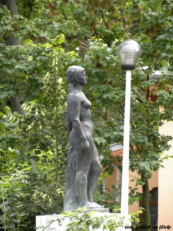 a statue stands next to a street light and trees