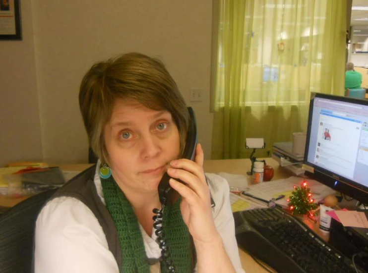 a woman with a scarf is on her phone while at her desk