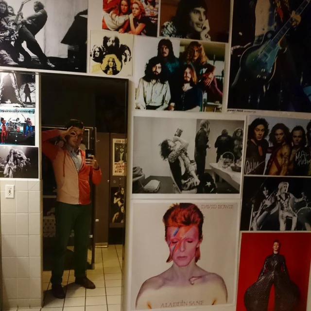 a man taking a po in a public restroom with pictures on the wall