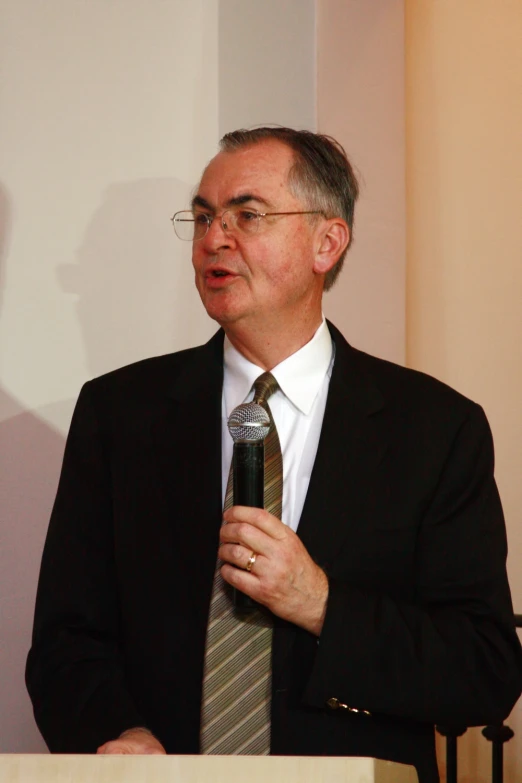 a man wearing glasses and a suit speaks into a microphone