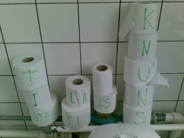 a bathroom with white toilet paper and green handwritten lettering on them