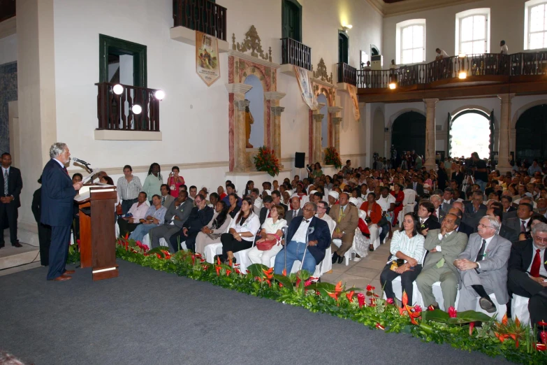 several people sitting in chairs and a man stands at the podium