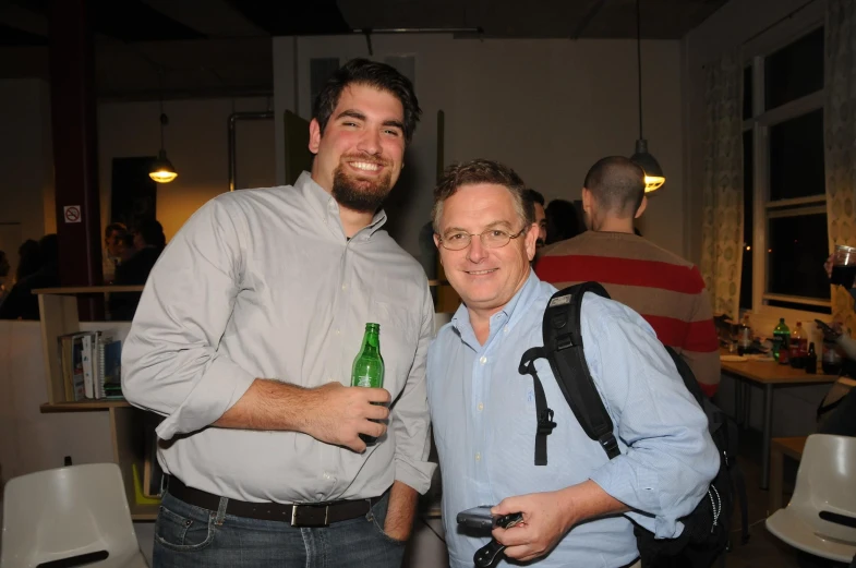 two men standing next to each other and holding bottles