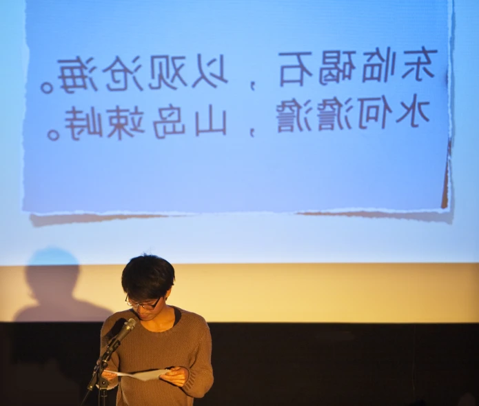 an asian woman stands in front of a podium, with a screen displaying the words