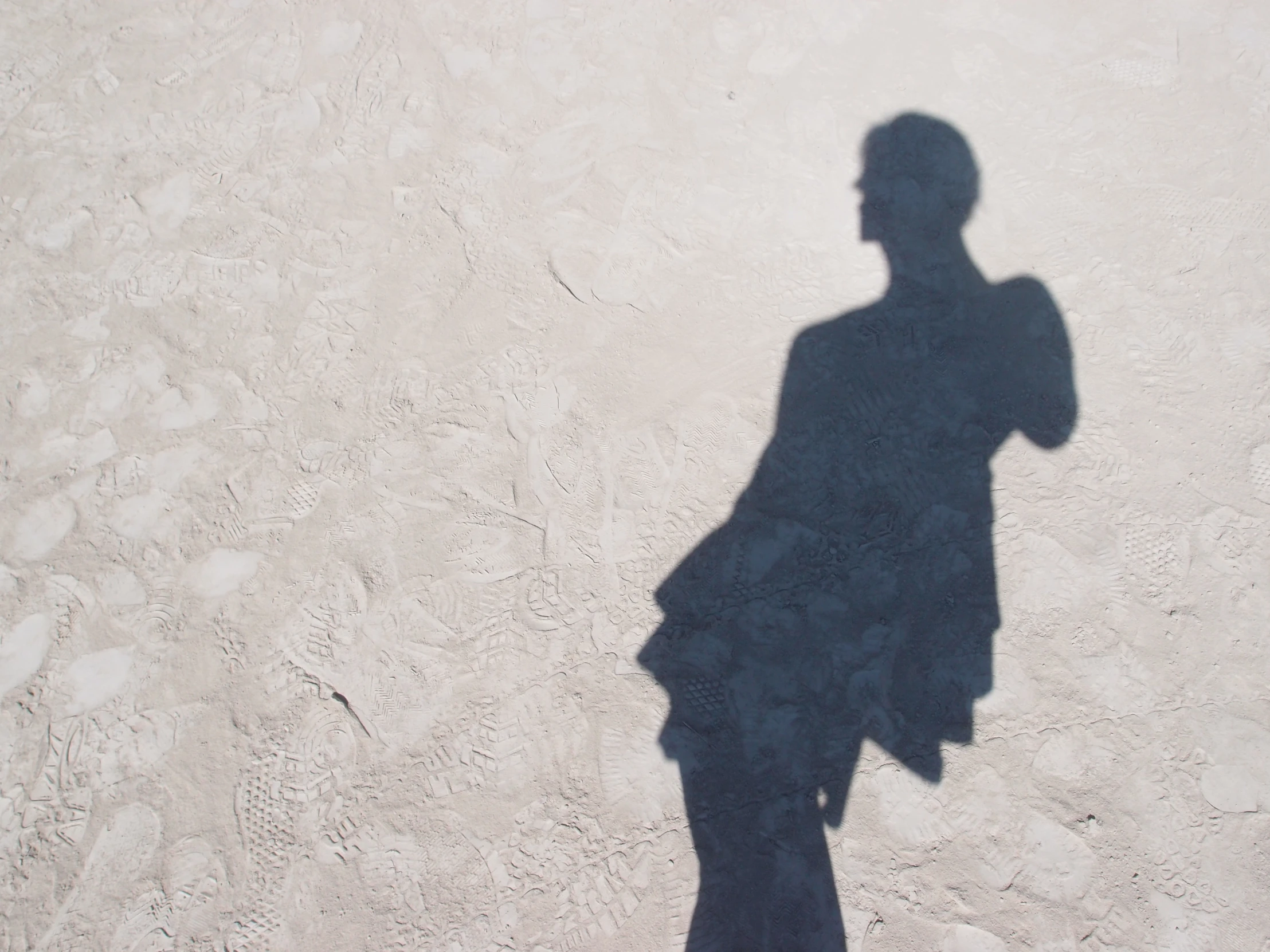 man standing with shadow on cement with black coat