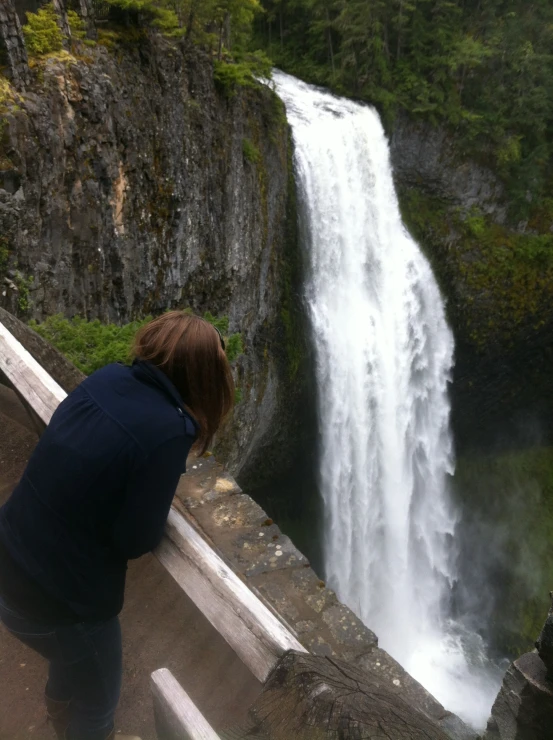 a woman at the edge of a walkway looking at a waterfall