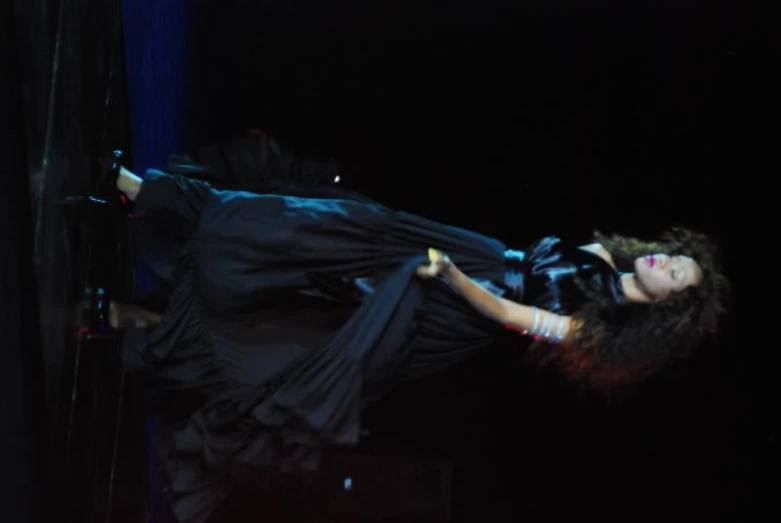 woman in black dress walking on stage at night