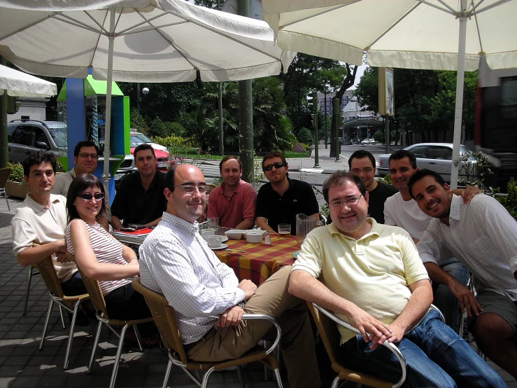 several men and women sitting around tables with umbrellas over them