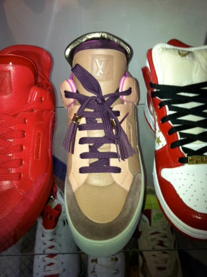 three different colored tennis shoes on display, with a purple ribbon and lace