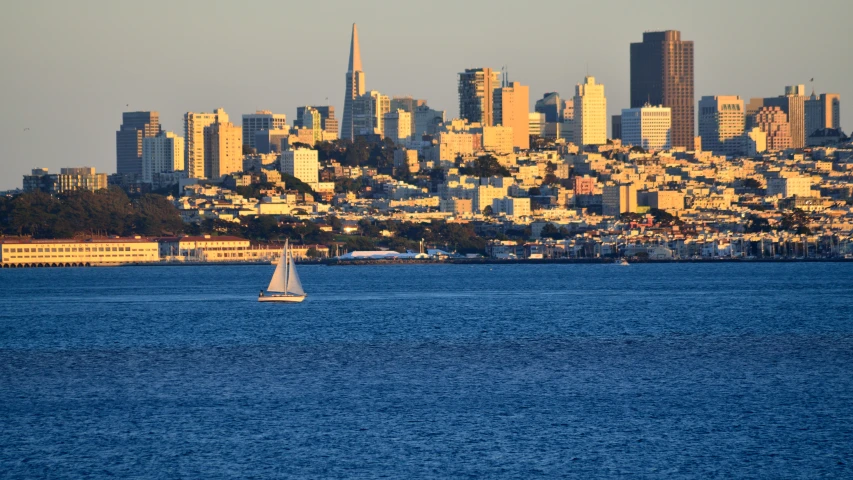 a sail boat in the ocean front with a city in the background