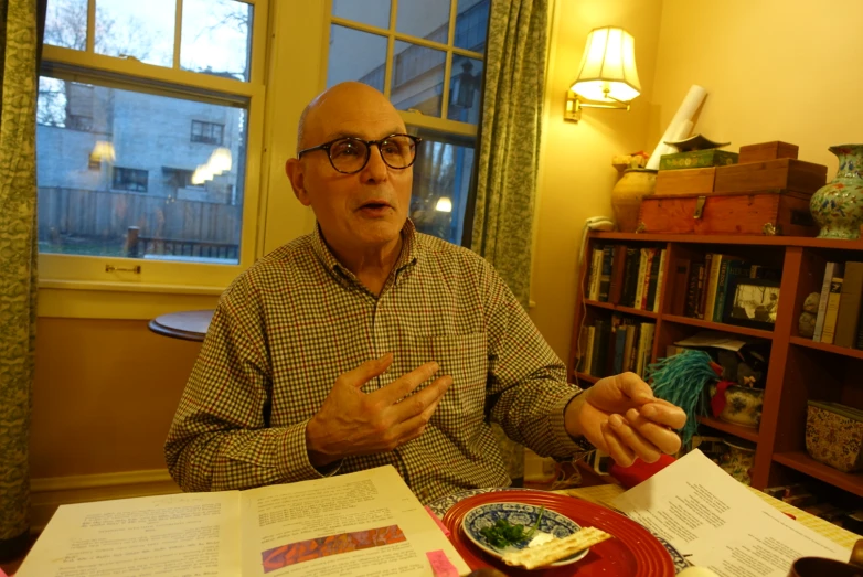 a balding man sits at a table with several books and papers