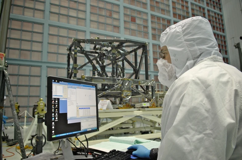 a man in white suit and goggles in front of a monitor