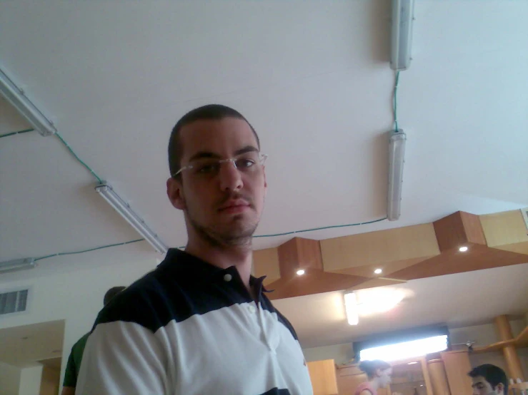 a man with glasses standing under an unfinished ceiling