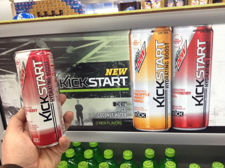 hand holding a can of kick start in front of stacks of six limeade and soda bottles
