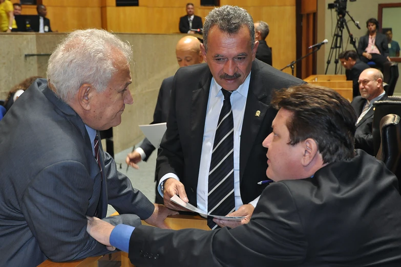 a man in business suit handing another person a paper