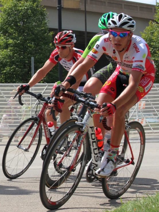 two men wearing helmets riding bicycles down a street