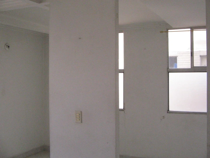 an empty white room with three windows and two different items on the floor