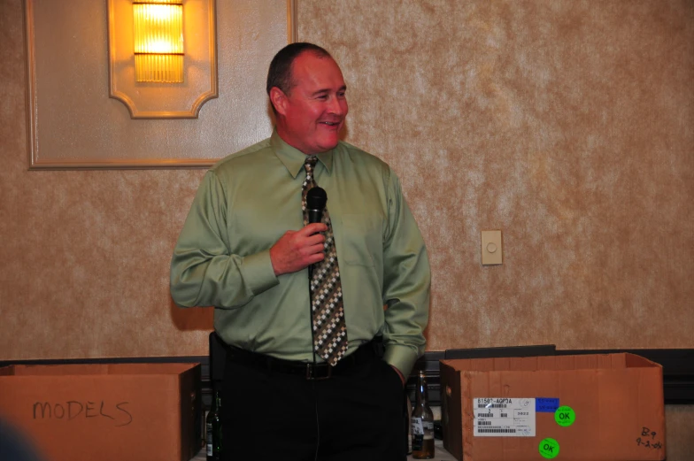 man in dress clothes stands near boxes and holds up his tie