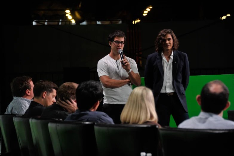 two people standing on stage speaking with other people