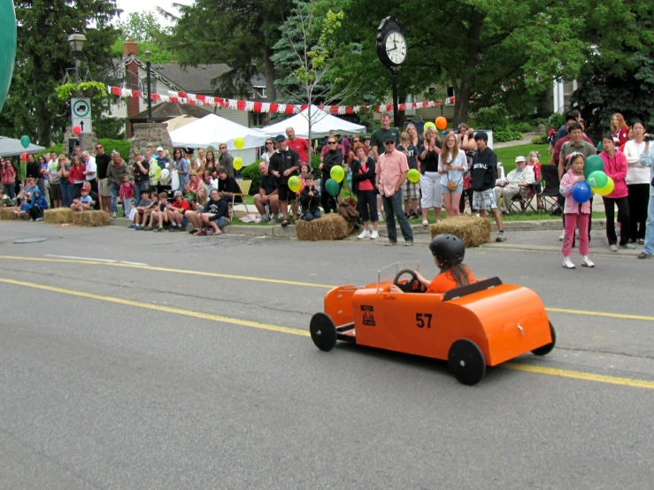 children drive an orange race car during the parade